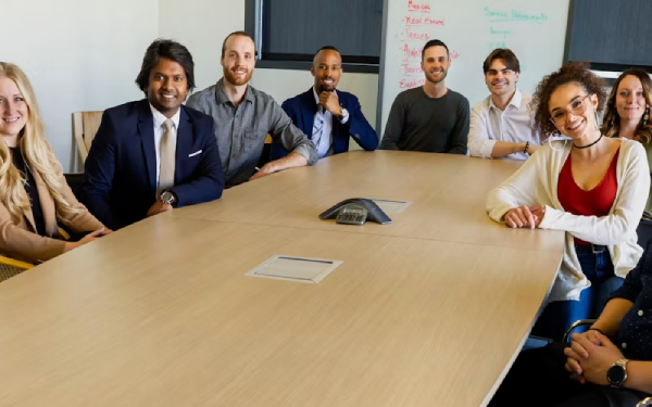 Three businesspeople smiling at a conference table with a speakerphone